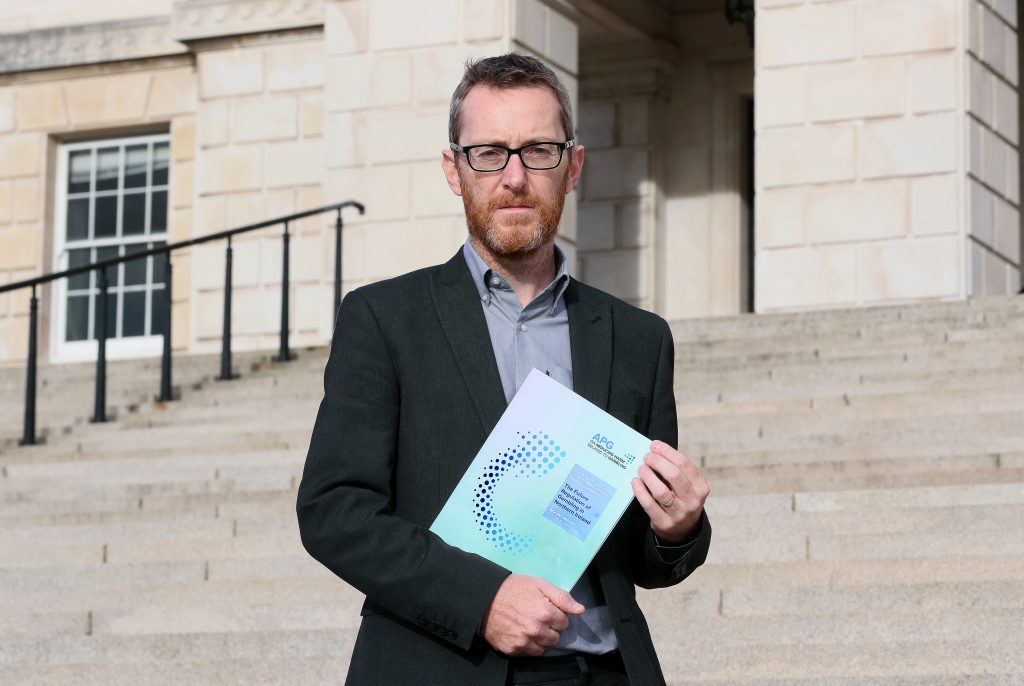 Chair of the All-Party Group, Philip McGuigan MLA, stands on the steps of Parliament Buildings at Stormont. He is holding a copy of the APG inquiry report.